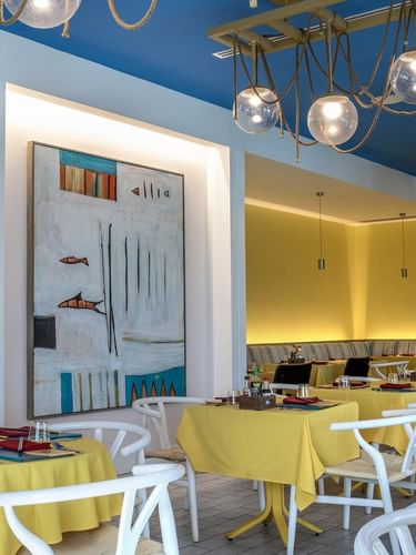 Yellow tables by white chairs under globe lights in Tings on a Stick painting at Warwick Paradise Island Bahamas