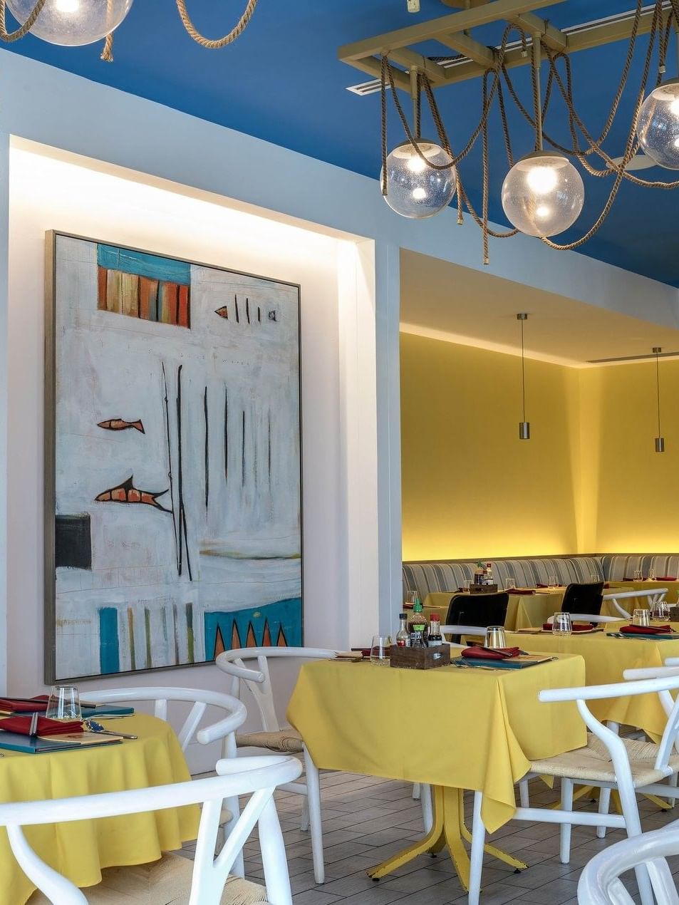 Yellow tables by white chairs under globe lights in Tings on a Stick painting at Warwick Paradise Island Bahamas