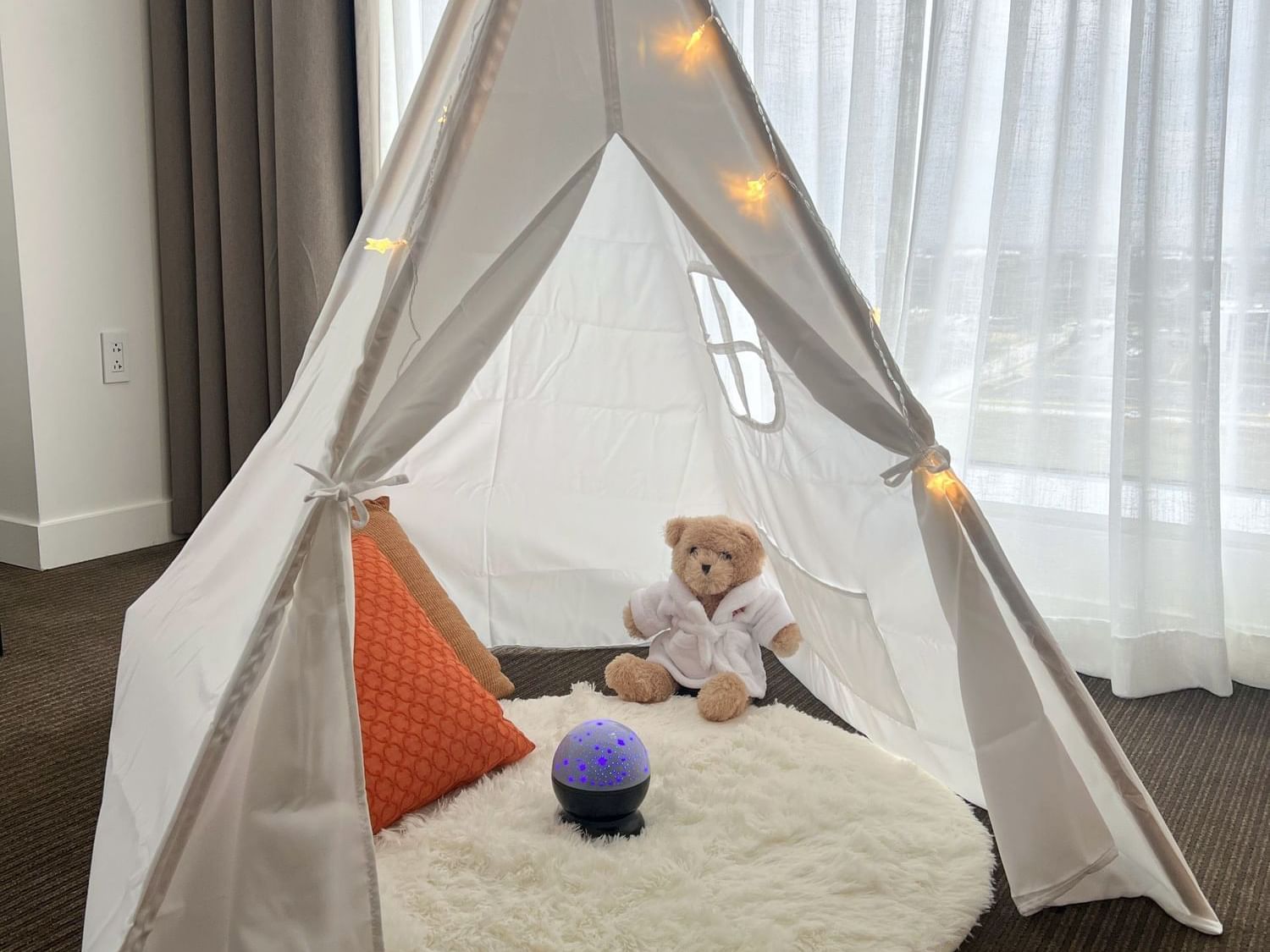 A white teepee tent with a teddy bear ready to welcome kids to enjoy the Little Campers Staycation package at the Hotel Arista in Naperville, IL.