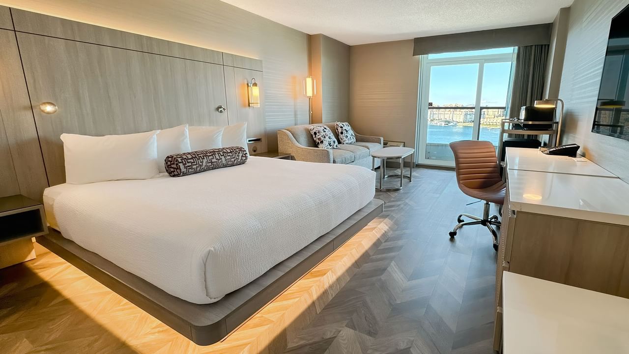 Hotel guestroom with king bed, sofa, TV, work desk, chair, and an ocean view