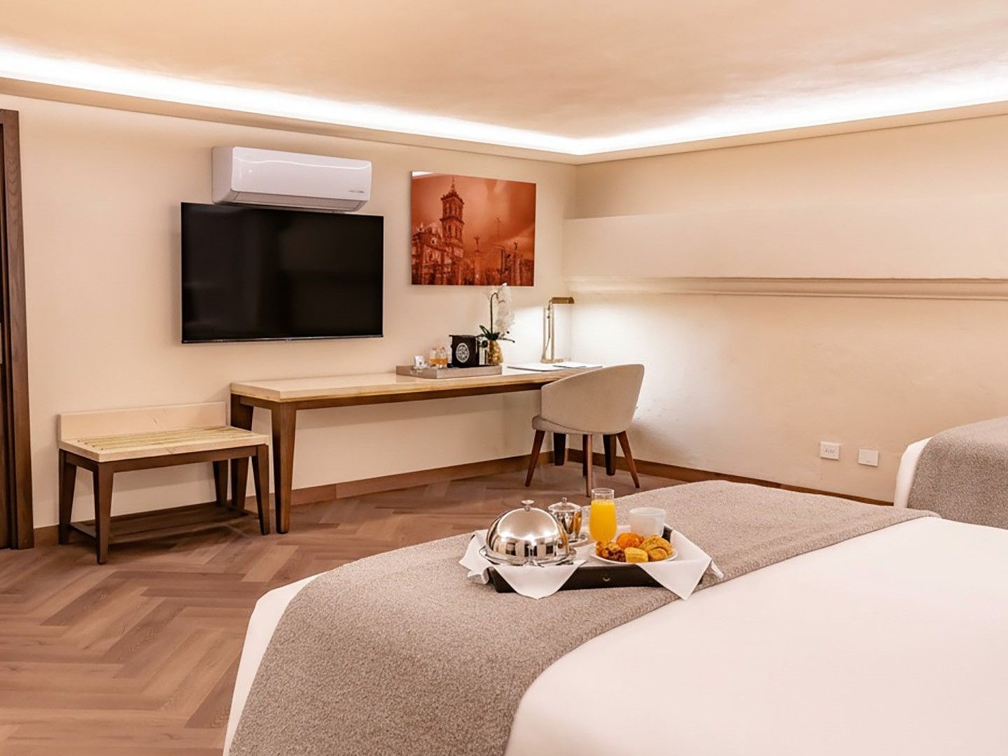 Habitación de hotel con dos camas, mesa de trabajo, televisor, y desayuno en bandeja.