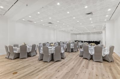 Modern ballroom with round tables, white linens, gray chairs, and wooden flooring at Riverwalk Plaza Hotel
