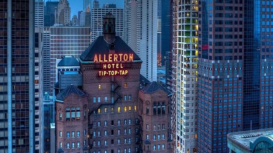 Exterior of the Warwick Allerton Chicago with a glowing sign near city skyscrapers
