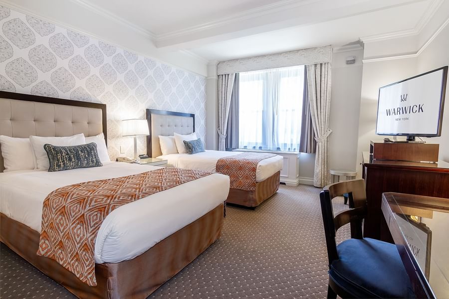 Two queen beds facing TV screen and desk area in Premier City View 2 Double Beds at Warwick New York