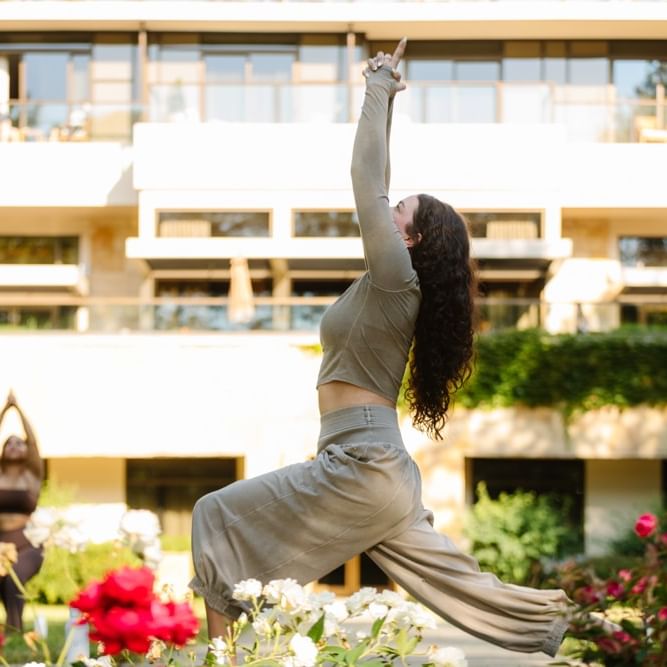 Woman practicing yoga outdoors in a garden with red flowers during Summer Wellness Series: Sunrise Morning Yoga.