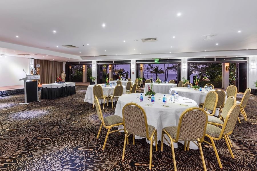Coral Coast Conference Centre with round tables and chairs by glass doors at Warwick Fiji Resort and Spa