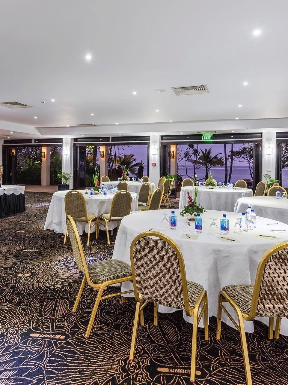 Coral Coast Conference Centre with round tables and chairs by glass doors at Warwick Fiji Resort and Spa