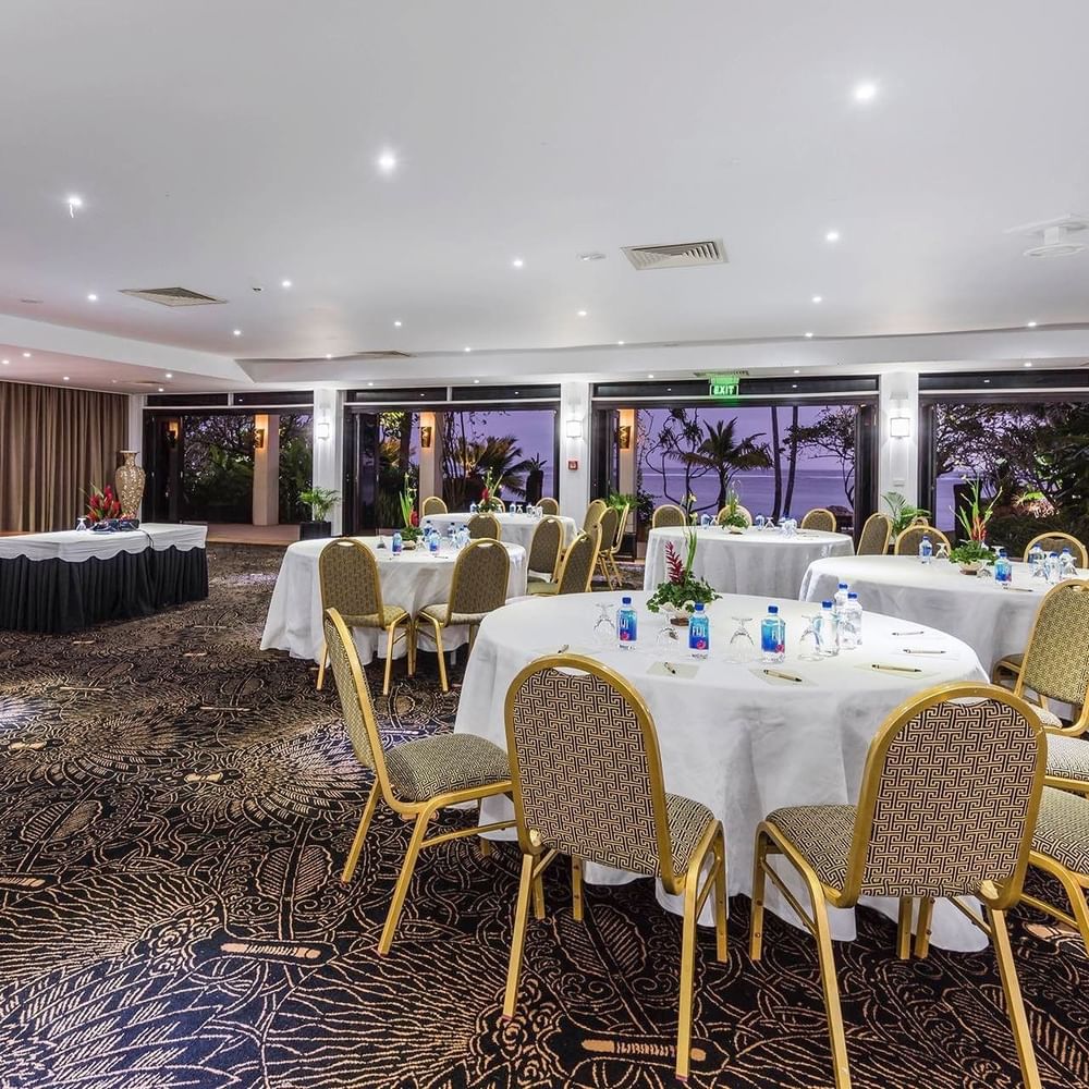 Coral Coast Conference Centre with round tables and chairs by glass doors at Warwick Fiji Resort and Spa