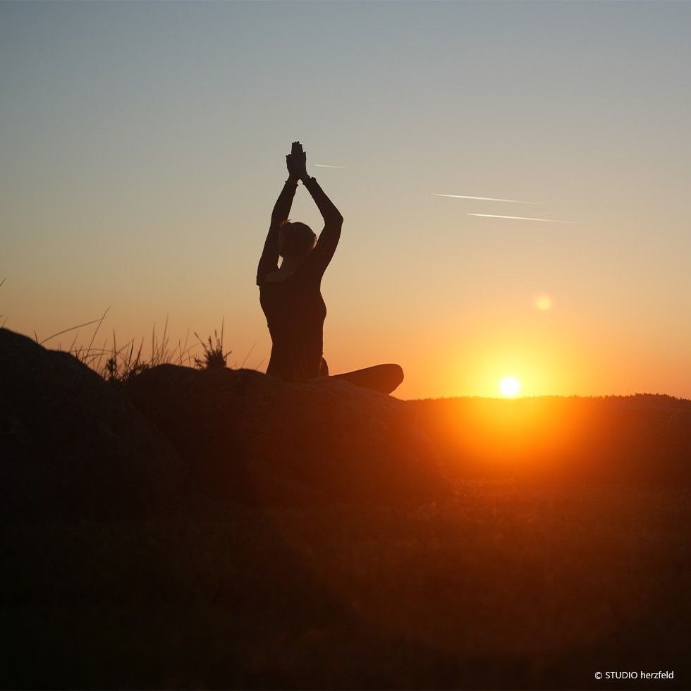 A person in yoga pose at sunset for the Summer Solstice offer.