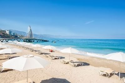 Sandy beach with white umbrellas and lounge chairs along turquoise ocean waters at Playa Los Arcos Puerto Vallarta 2023