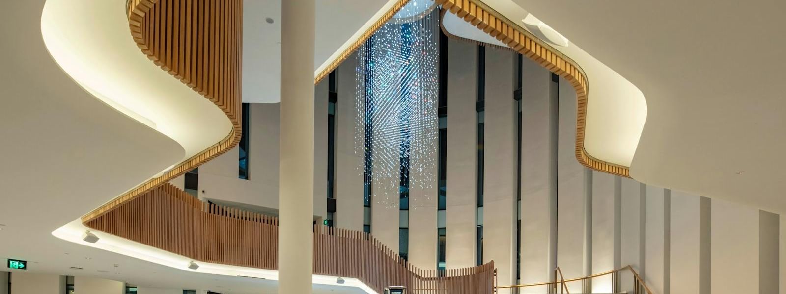 A modern interior with curved wooden stairs, a central column, a crystal chandelier, and a reception desk.