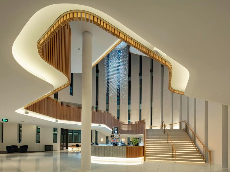 A modern interior with curved wooden stairs, a central column, a crystal chandelier, and a reception desk.