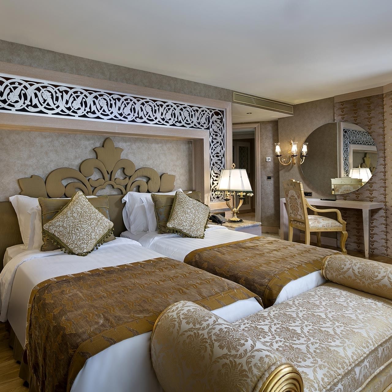 Lake House im Titanic Mardan Palace – zwei Betten, verziertes Kopfteil, Nachttischlampen, Liegestuhl, Spiegel, Stuhl und Schreibtisch.