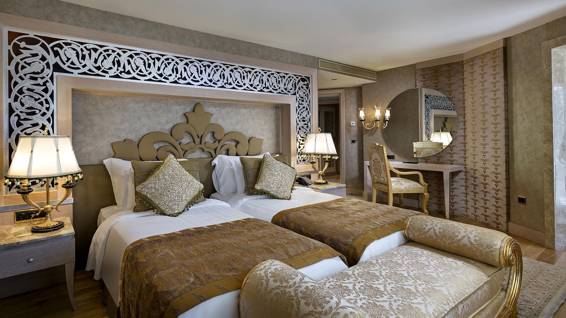 Lake House im Titanic Mardan Palace – zwei Betten, verziertes Kopfteil, Nachttischlampen, Liegestuhl, Spiegel, Stuhl und Schreibtisch.