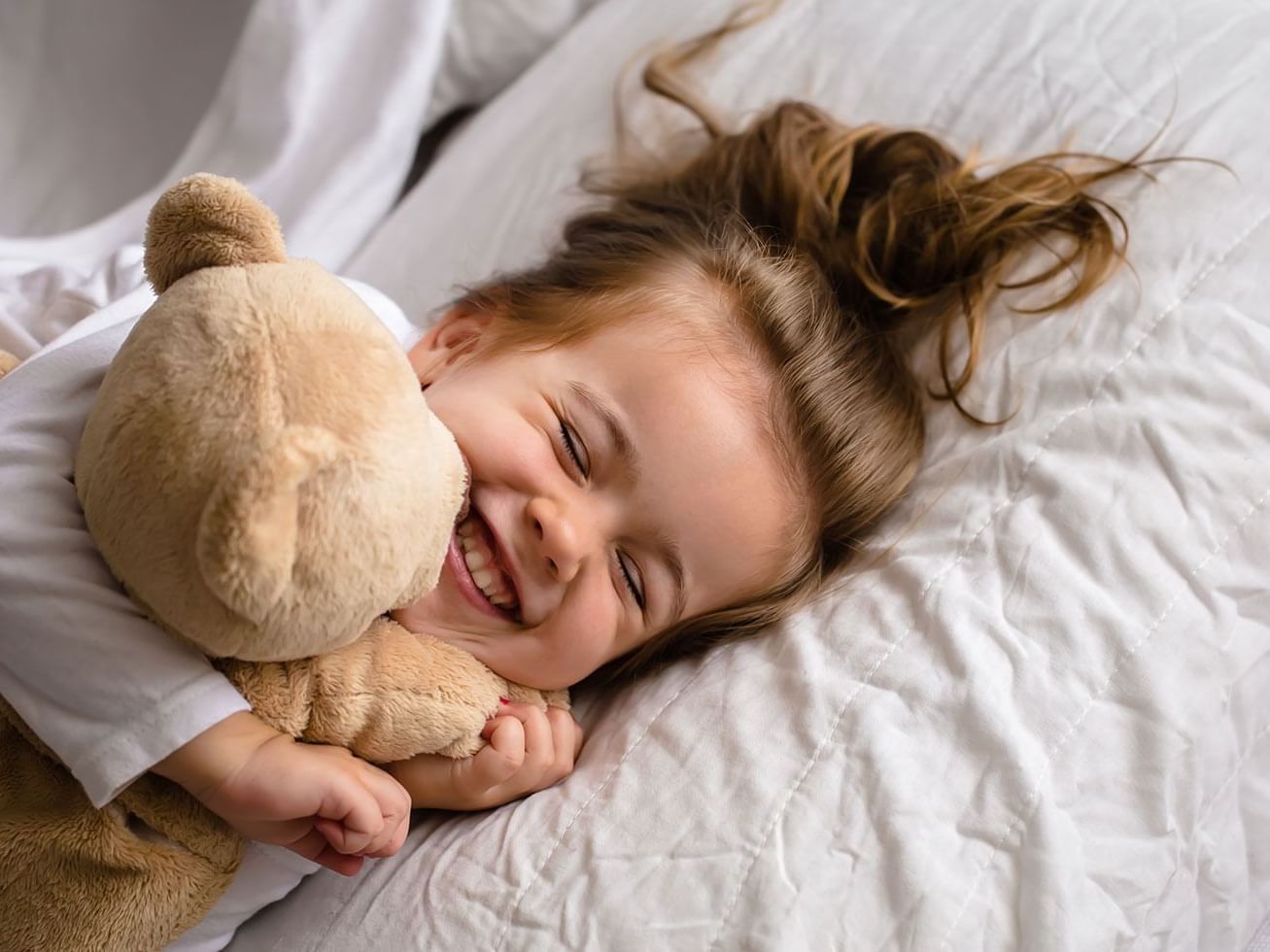 A kid cuddling with a stuffed teddy bear on a bed