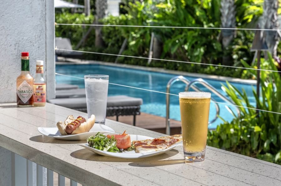Hot dog and pizza by a beer surrounding a pool area in Chickcharnie's Pizzeria & Grille at Warwick Paradise Island Bahamas
