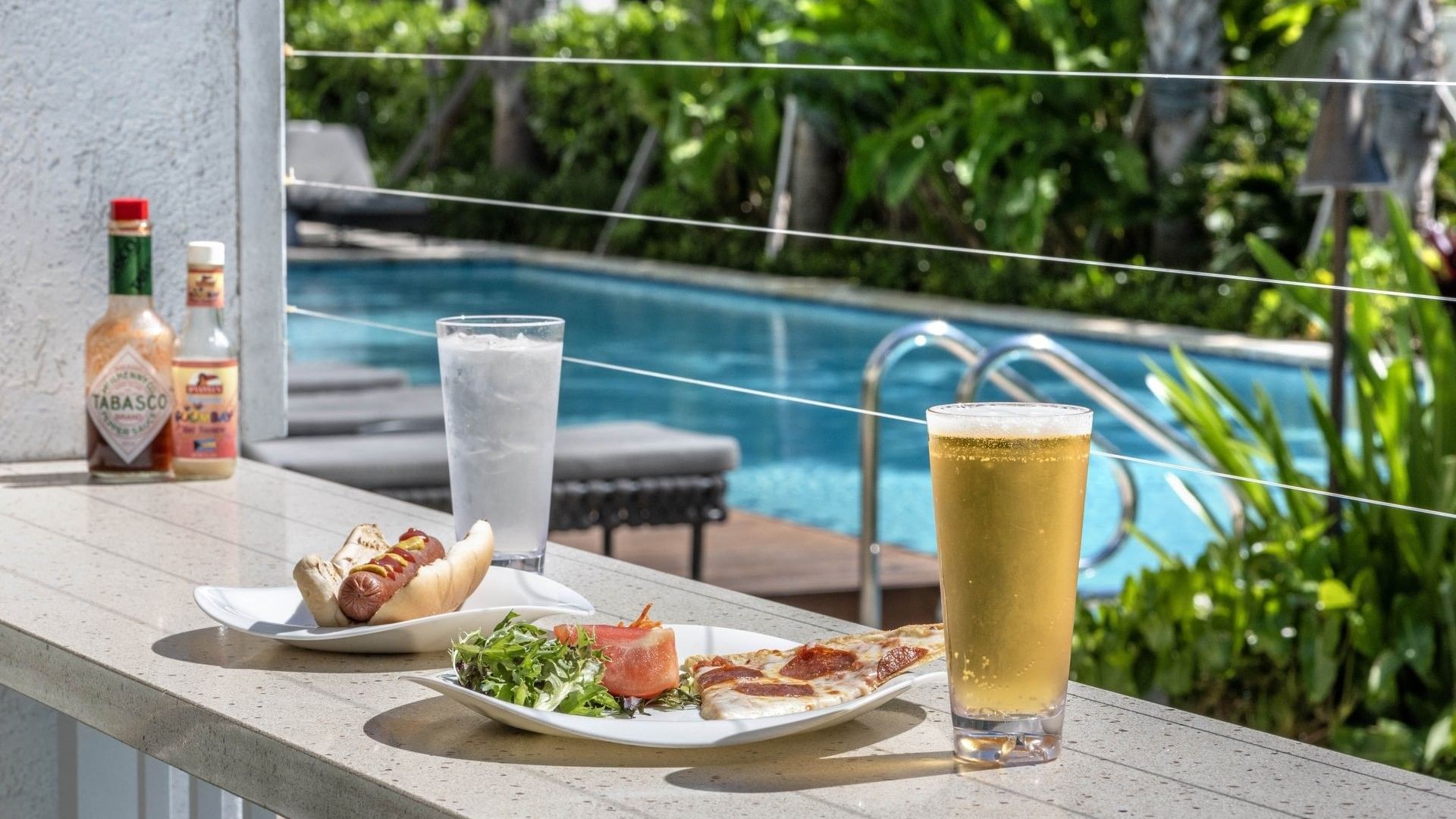 Hot dog and pizza by a beer surrounding a pool area in Chickcharnie's Pizzeria & Grille at Warwick Paradise Island Bahamas