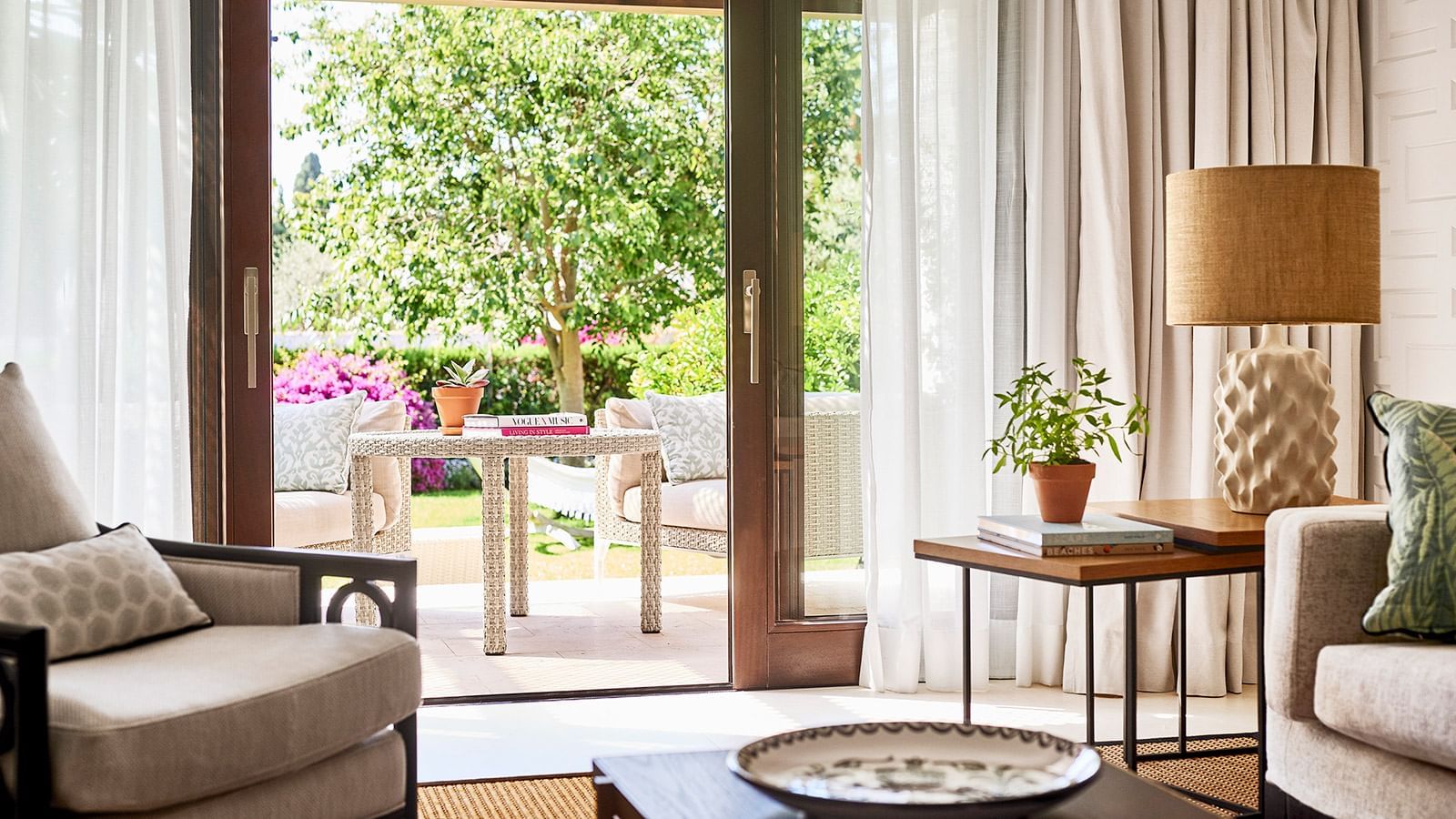 Junior Suite Deluxe living room with open sliding doors revealing a sunny patio and lush green garden at Marbella Club