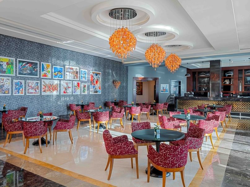 A luxurious restaurant with tables, chairs, artwork on walls, and orange chandeliers hanging from the ceiling.