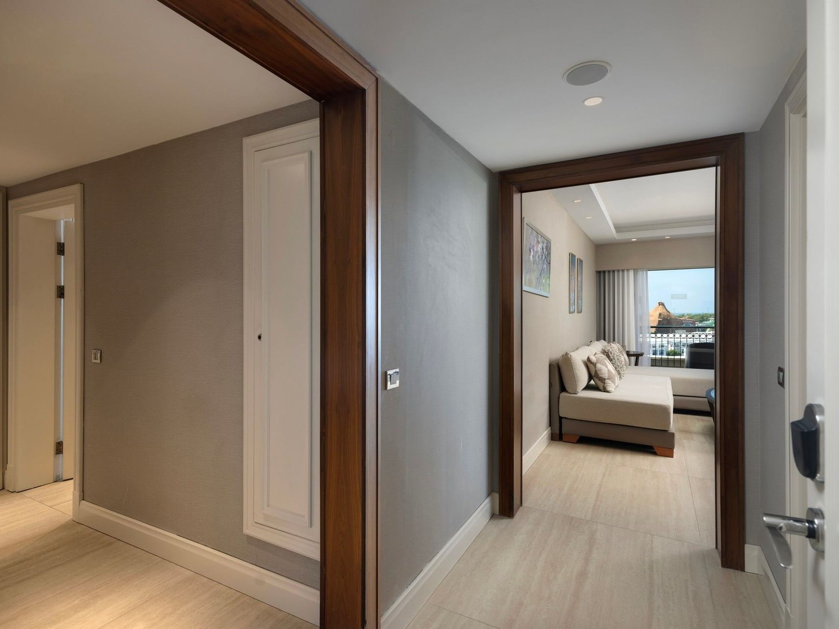 Modern hotel suite hallway with light wood floors leading to bedroom with balcony view at Titanic Deluxe Golf Belek