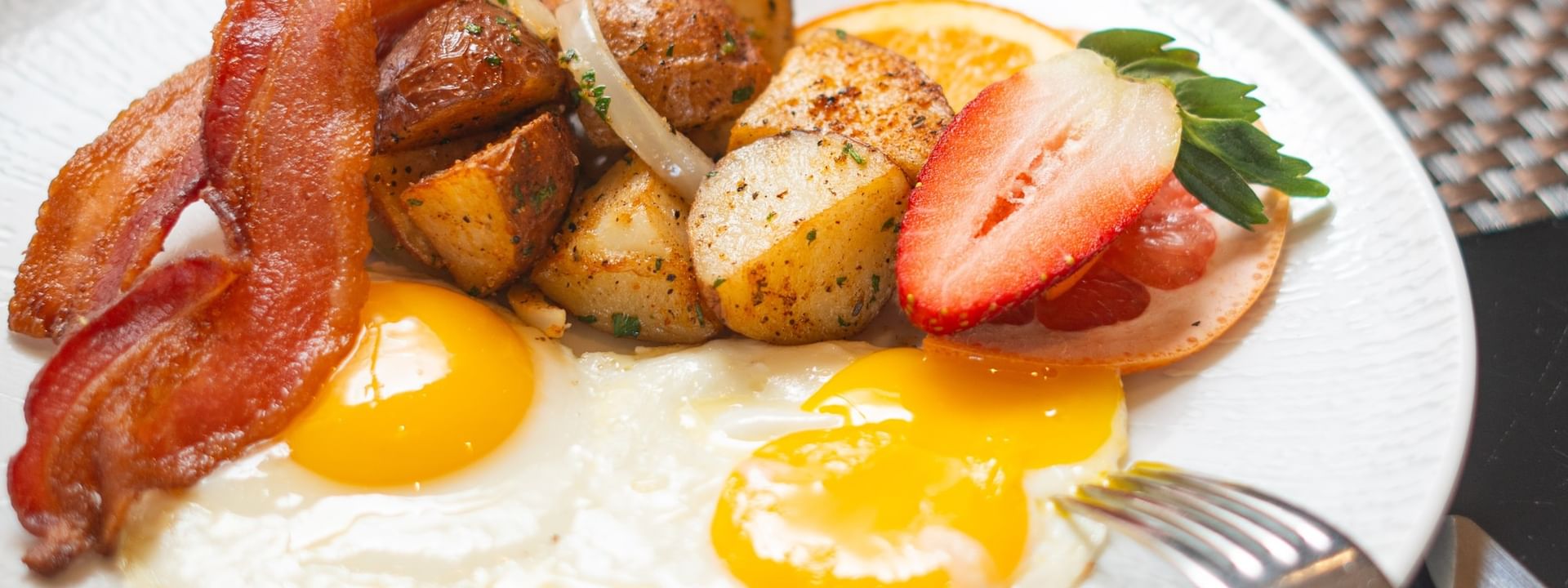 Fried eggs with crispy bacon and potatoes under a fresh strawberry in The Landmark - Breakfast at Warwick Melrose Dallas