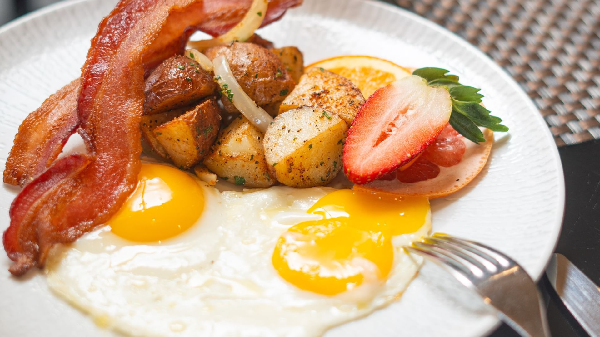 Fried eggs with crispy bacon and roasted potatoes under fruit slices in The Landmark - Breakfast at Warwick Melrose Dallas