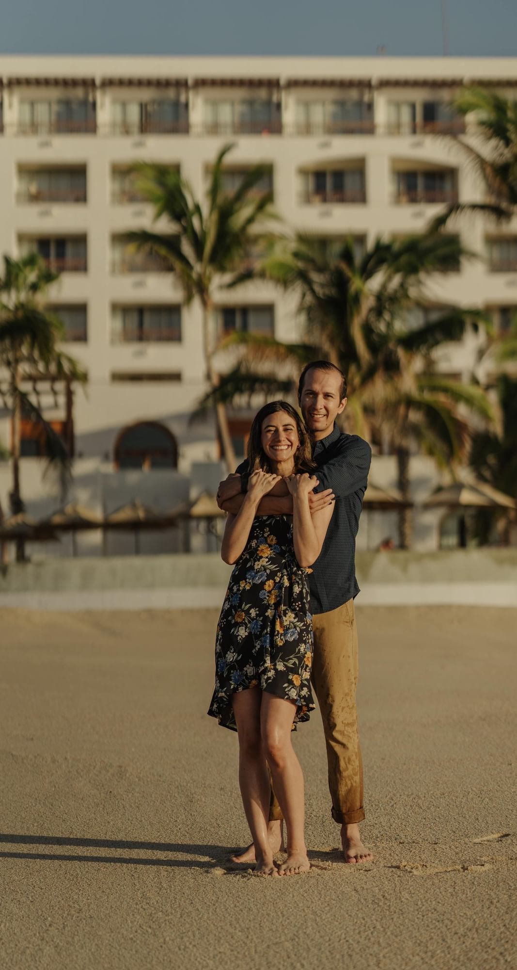 Couple hugging on beach in front of the Marquis Los Cabos Hotel in Mexico.
