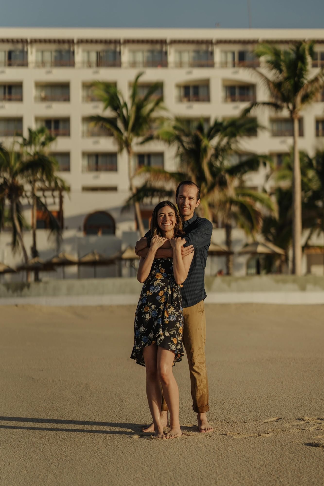Couple hugging on beach in front of the Marquis Los Cabos Hotel in Mexico.