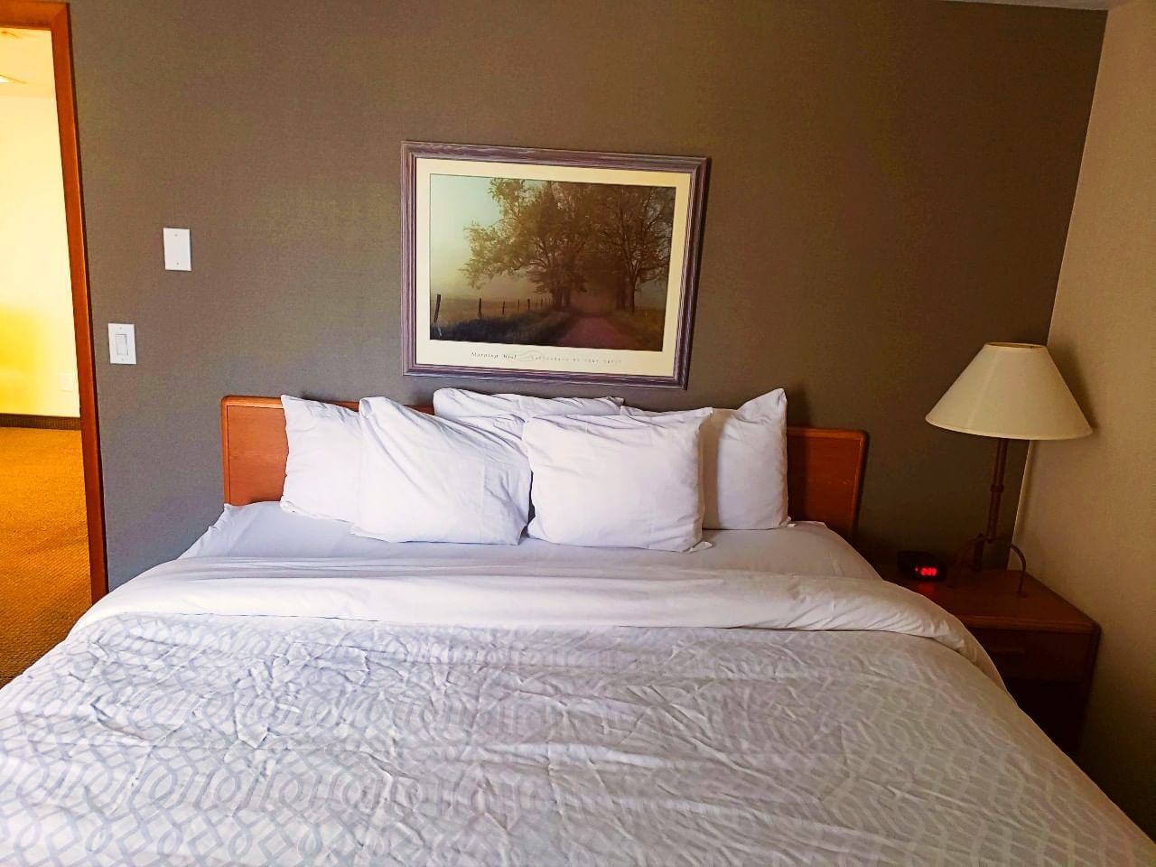 King bed with white bedding and pillows, nightstand with lamp, and painting at Evergreen Resort in Cadillac.