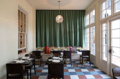 Elegant dining room with dark wood tables, green velvet curtains, and colorful tiled flooring at The Ashbrook Hotel