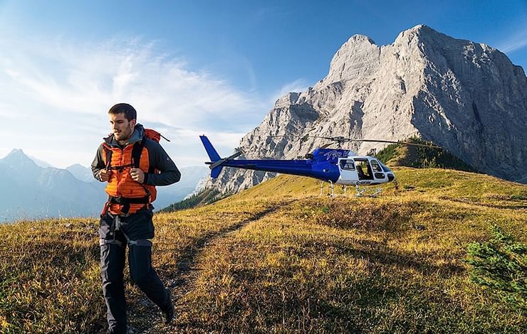 A man walking on a hill with a helicopter in the background near Blackstone Mountain Lodge