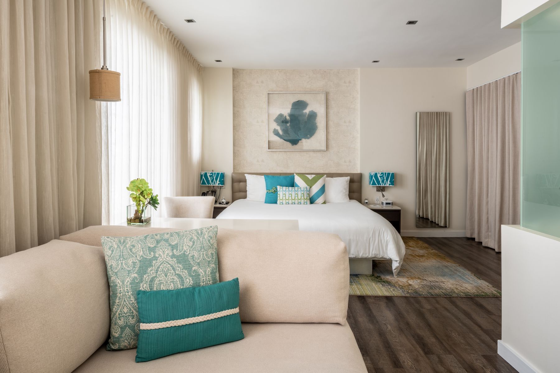 A wide view of a hotel room with a beige sofa, a bed with white linens, and a colorful rug.