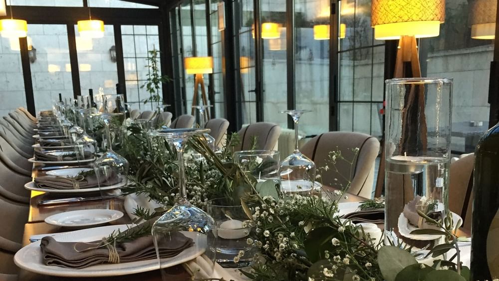 Long table with glasses by green plants surrounding a formal dinner setup in Maple Tree Restaurant at Warwick Ankara