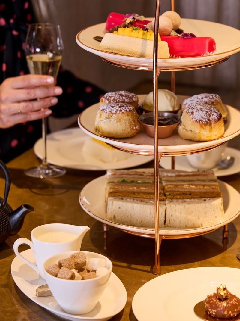 People enjoying a three-tiered assortment of cakes, scones and sandwiches with champagne in May Fair Kitchen