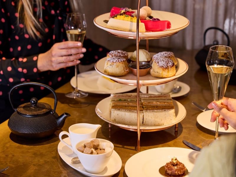 People enjoying a three-tiered assortment of cakes, scones and sandwiches with champagne in May Fair Kitchen