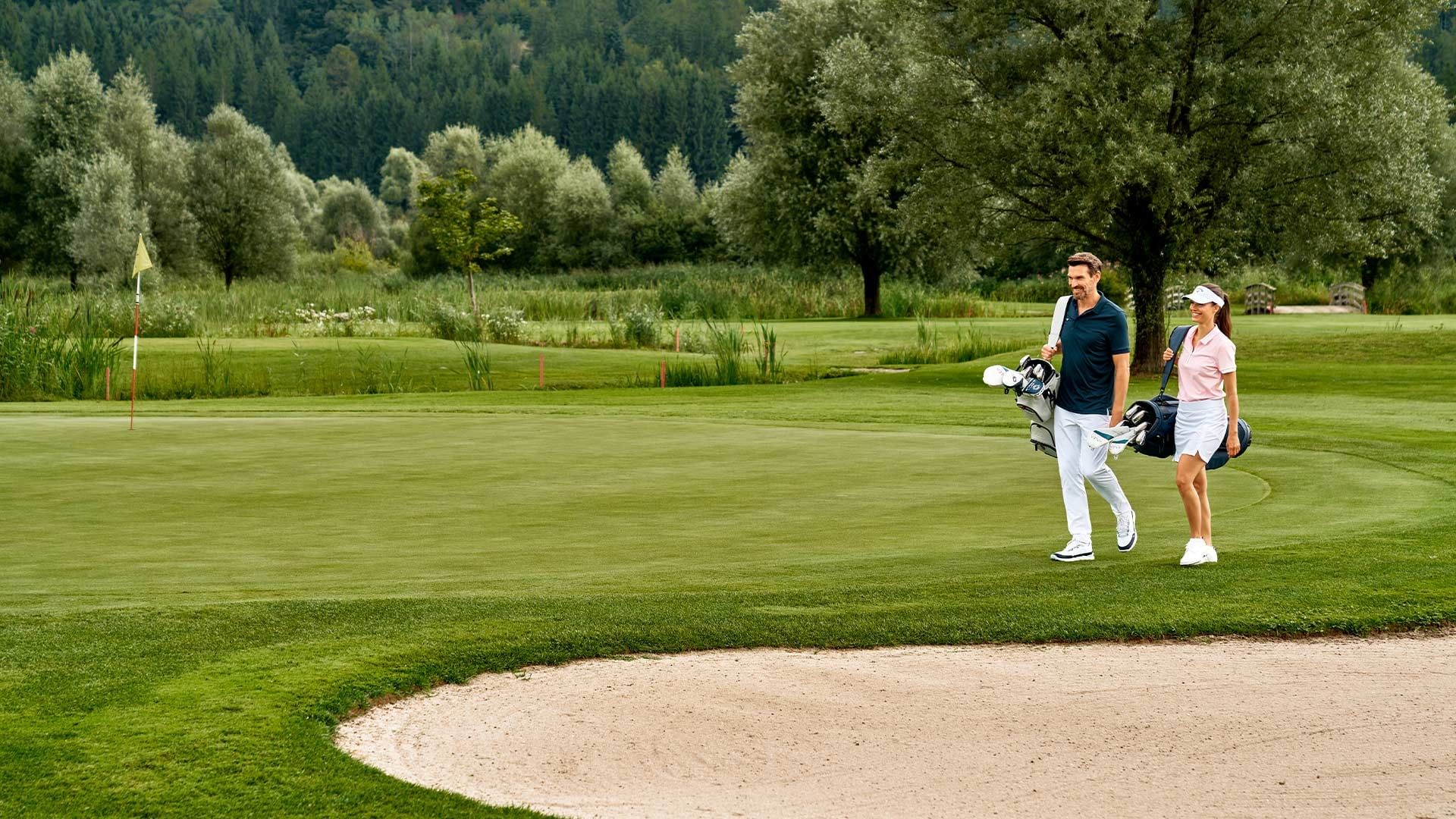 Couple walking with golf clubs on golf course at Falkensteiner Balance Resort Stegersbach