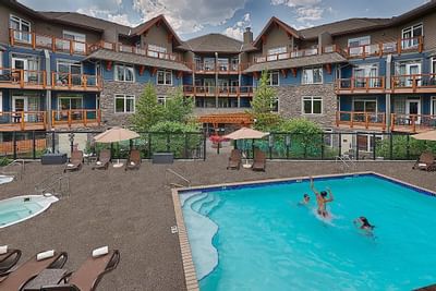 Family swimming in the outdoor pool surrounded by lounge chairs and umbrellas at Blackstone Mountain Lodge