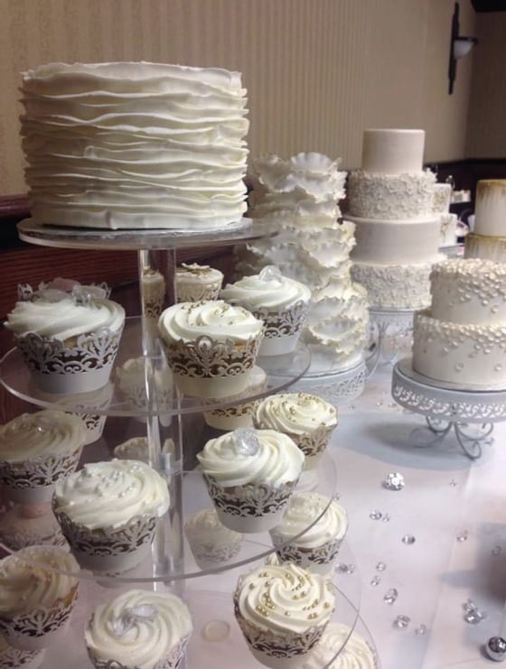 White ruffled wedding cake by Cupcakes on a tiered stand, surrounded by cake displays at Glenmore Inn & Convention Centre
