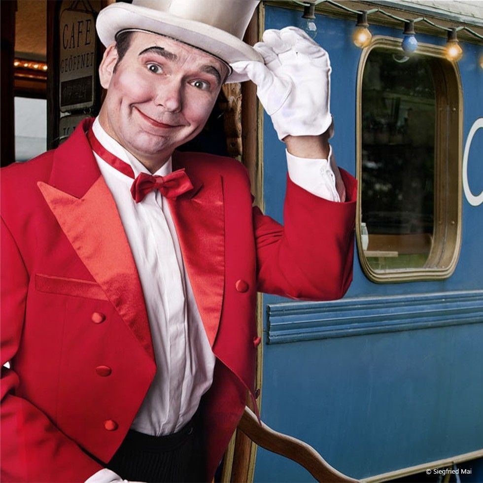 Mann in roter Anzug und Zylinder auf dem Kopf beim Varietéabend mit Herrn Mai.