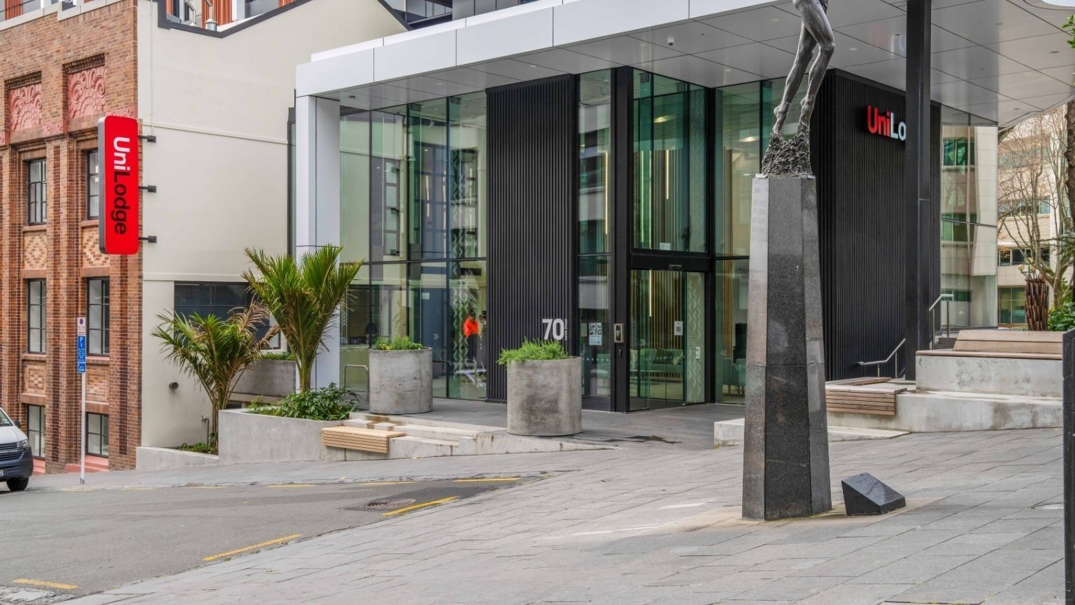 Modern glass entrance with concrete planters and sculpture at UniLodge Auckland Central