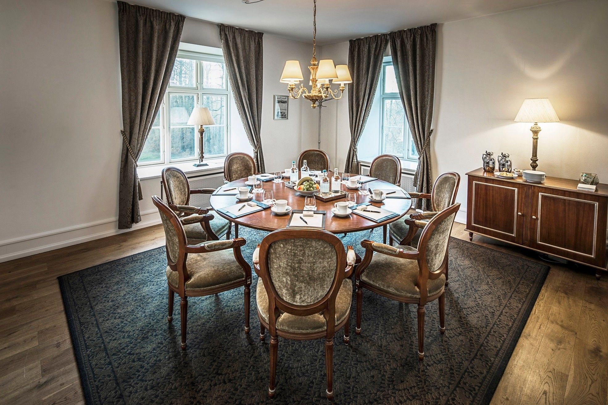 Classic round wooden boardroom table featuring plush chairs and patterned rug with classic chandelier at Warwick Denmark