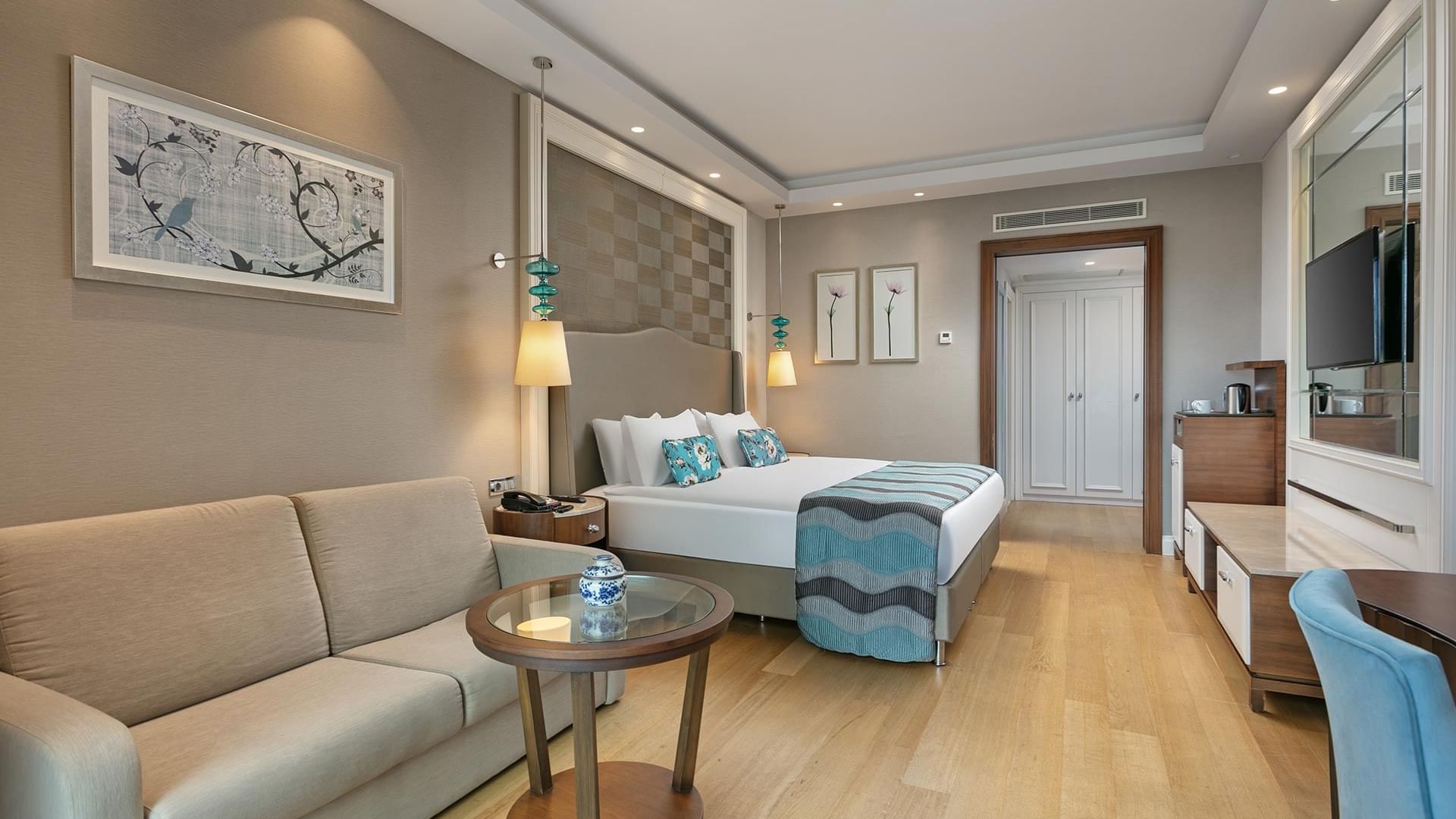 Titanic Deluxe Golf Belek’te Aile Odası’nda yatak yanında modern mobilyalarla TV ve oturma alanı.