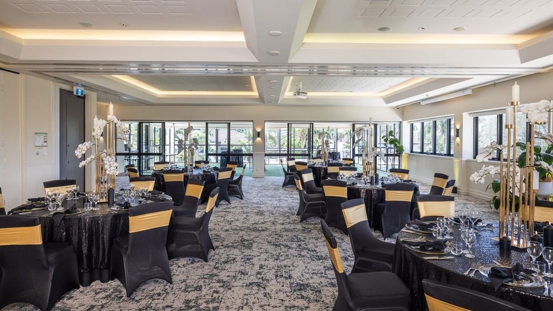 A banquet hall with black and yellow chairs, black tablecloths, and white floral centerpieces on tables.
