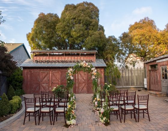 Outdoor wedding ceremony setup with floral arch and wooden chairs on brick patio at Cambria Pines Lodge