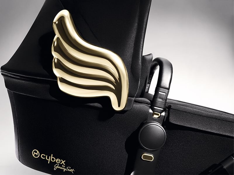 Gold wing emblem on a black bassinet hood, beside a leather handle and clip on a Cybex stroller at Hotel X Toronto