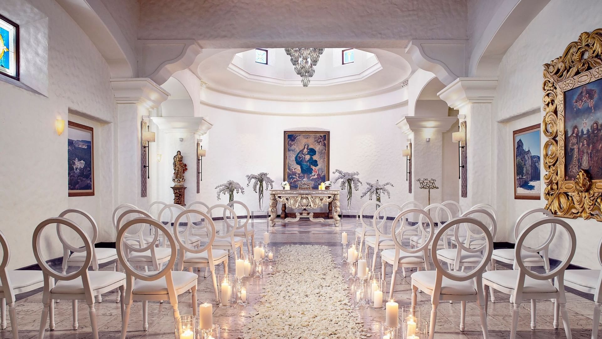 Impresionantes arreglos de boda en interiores en la Capilla de Hacienda del Mar Los Cabos, decorada con pétalos de rosa blanca y velas