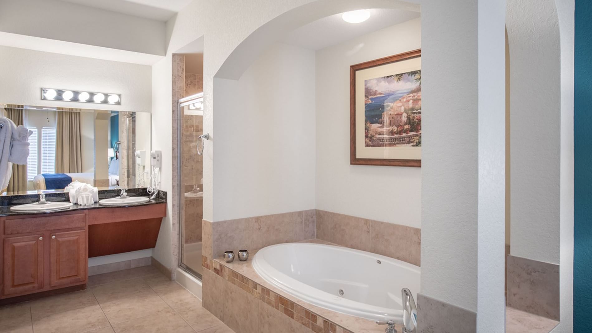 A bathroom with a large bathtub, shower, double vanity, and artwork on the wall.