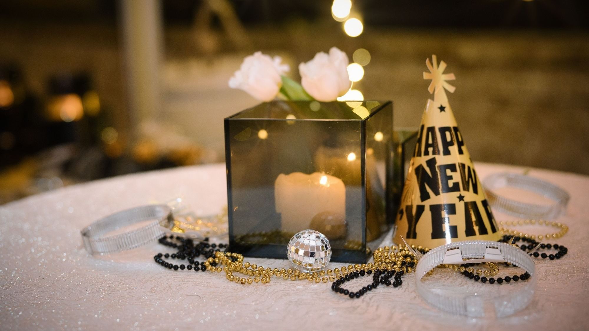A table with a glass box containing a candle, flowers, and a New Year party hat.