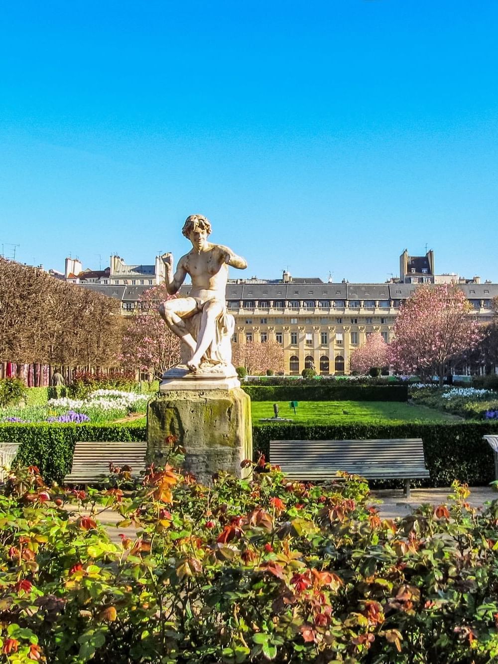 Stone statue on a pedestal by wooden benches under a clear blue sky at Warwick Paris Champs Elysées