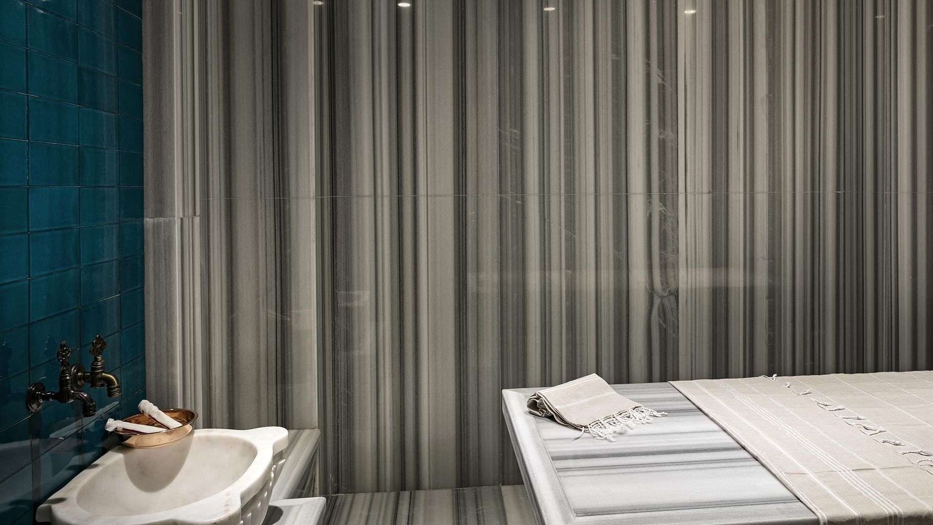 A luxurious bathroom with a white sink, blue tiles, striped walls, and a table covered with a towel.
